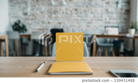 bright yellow notebook and pen on wooden desk in modern office setting, with blurred background of chairs and tables, creating calm and productive atmosphere 130431488