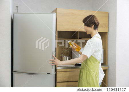 A woman in an apron opening a refrigerator 130431527
