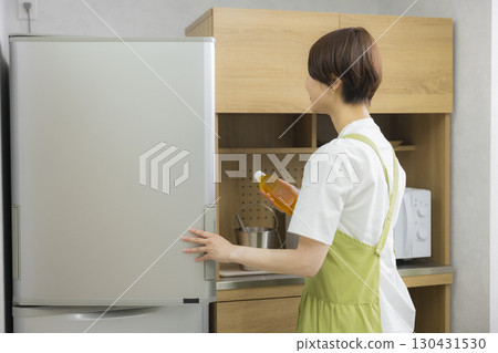 A woman in an apron opening a refrigerator 130431530