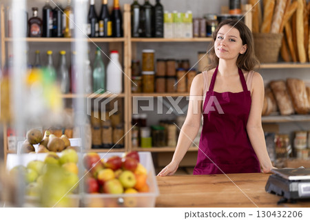 Young saleswoman is standing at the counter in grocery store Young saleswoman is standing at the counter in grocery store 130432206
