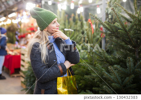Woman choose christmas tree at street fair Woman choose christmas tree at street fair 130432383