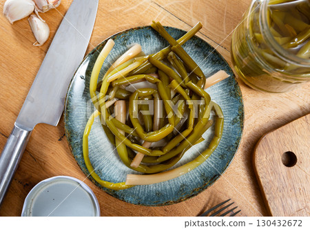 Pickled ramson is laid out on plate, next to it is cutting board, garlic cloves, knife and cutting board Pickled ramson is laid out on plate, next to it is cutting board, garlic cloves, knife and cutting board 130432672