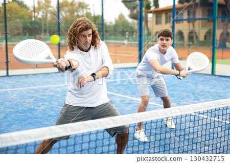 Focused men of different ages playing padel on hard court 130432715