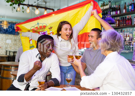 Excited diverse soccer supporters with flag of Spain celebrating victory with pint of beer in the pub Excited diverse soccer supporters with flag of Spain celebrating victory with pint of beer in the pub 130432857