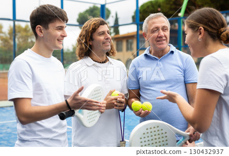 Four paddle tennis players talking on court 130432937