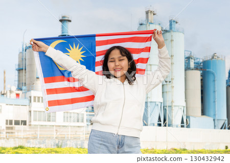 Happy young woman with flag of Malaysia against background of factory 130432942
