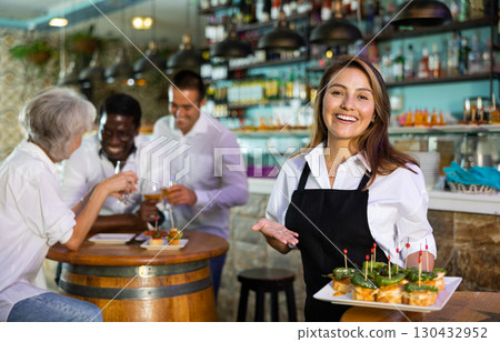 Cheerful smiling female waiter holding served tray meeting visitors at bar Cheerful smiling female waiter holding served tray meeting visitors at bar 130432952