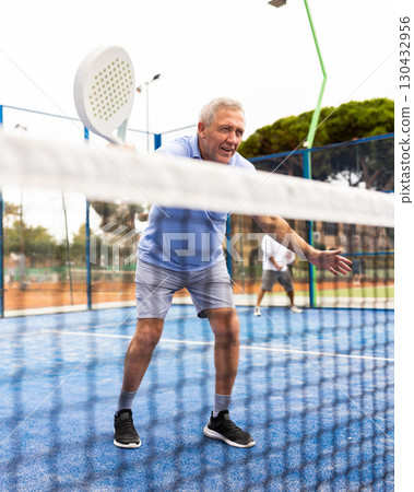 Aged man playing paddleball match on outdoor court 130432956