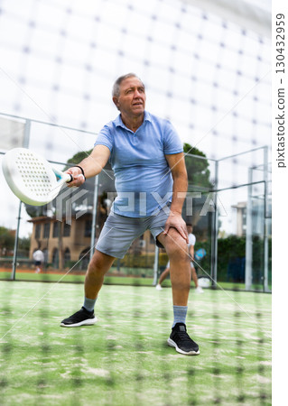 View through tennis net of elderly man playing paddle tennis 130432959