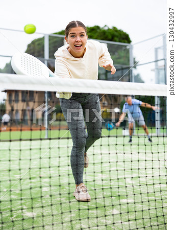 Emotional young European girl padel player hitting ball with racket on hard court in autumn 130432997