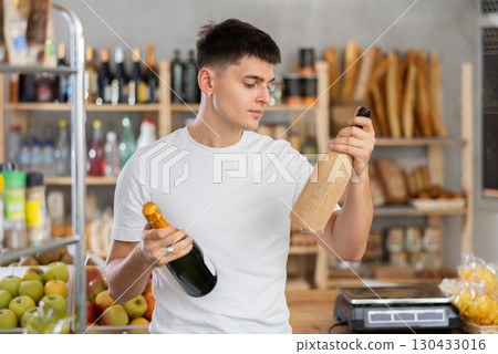 Guy carefully chooses spark wine or traditional wine in grocery store 130433016