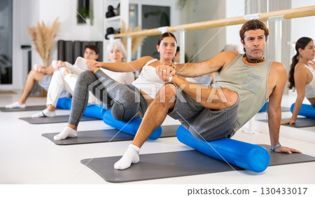 Women and men doing stretching workout during group training in yoga class 130433017