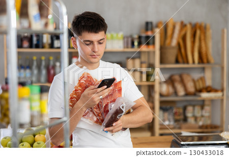 Young guy is scanning QR on dried sausage and meat in grocery store 130433018