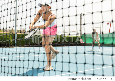 Sporty girl tennis player playing tennis. View through tennis net 130433023