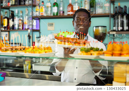 Bartender working behind counter in bar, presenting fresh sandwiches pinchos 130433025