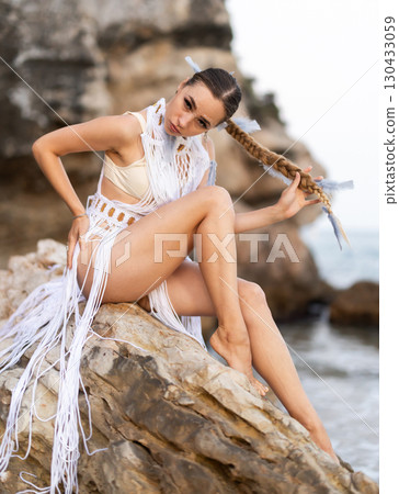Girl on seashore in sexy and revealing carnival costume sitting on stone 130433059