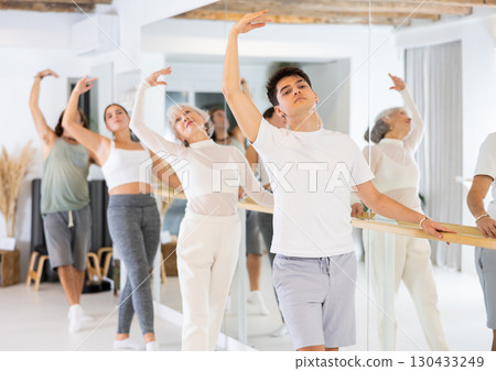Young dancer man exercise near the ballet barre at a group training session in classical dance school. Young dancer man exercise near the ballet barre at a group training session in classical dance school. 130433249