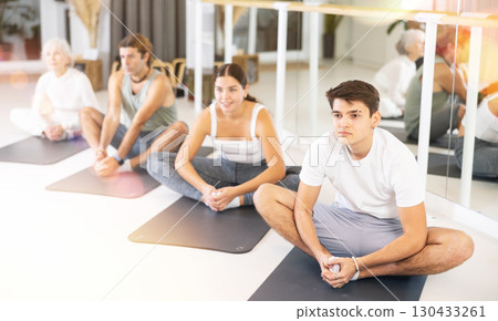 Young man practicing pilates on gray mat in gym room 130433261
