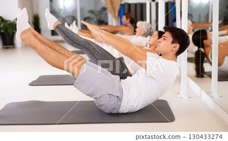 Young man practicing pilates on gray mat in gym room 130433274
