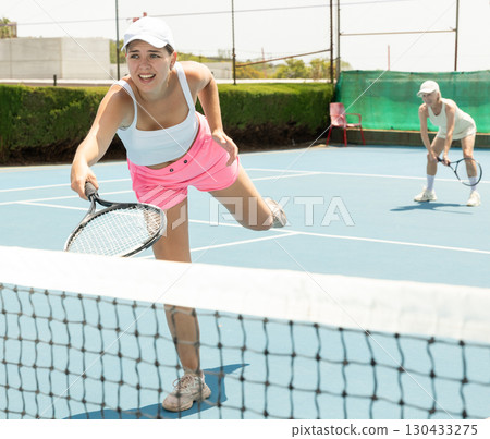 Young woman playing tennis with her teammate in court 130433275