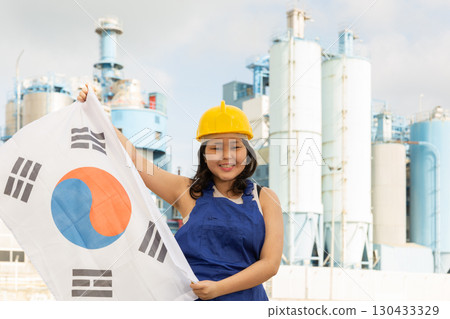 Portrait of teenage girl in blue overalls with flag of South Korea in her hands against the backdrop of modern metallurgical plant 130433329