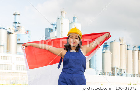 National flag of Indonesia in the hands of girl in overalls against background of modern metallurgical plant 130433372