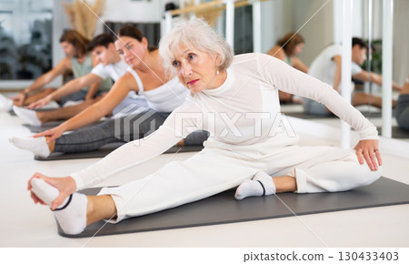 Elderly woman practicing pilates on gray mat in gym room 130433403