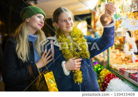 Teenage girl with mother looking for decorations on Christmas street market 130433409