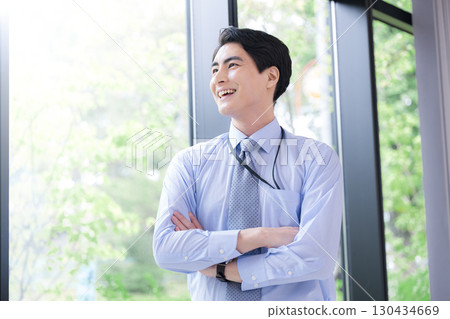 A businessman thinking by the window with his arms crossed and a smile on his face. A positive image of success, trust, and looking up to the future. 130434669