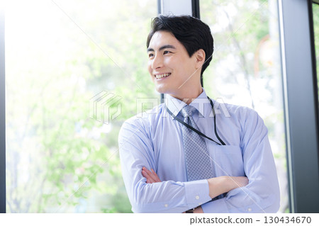 A businessman thinking by the window with his arms crossed and a smile on his face. A positive image of success, trust, and looking up to the future. A businessman thinking by the window with his arms crossed and a smile on his face. A positive image of success, trust, and looking up to the future. 130434670