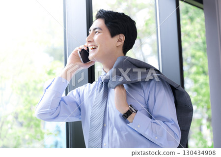 一位西裝革履的商人在綠樹成蔭的窗邊打電話的照片 一位西裝革履的商人在綠樹成蔭的窗邊打電話的照片 130434908