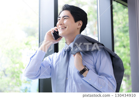 Image of a business man in a suit making a phone call by a window with fresh greenery 130434910