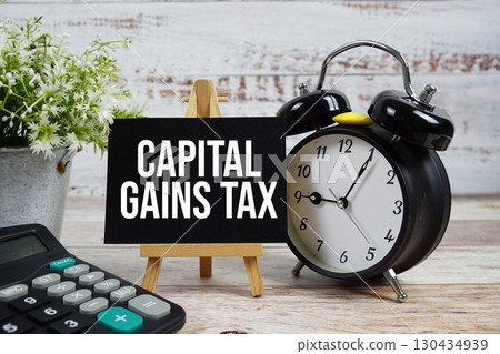 Capital Gains Tax text with alarm clock and calculator on wooden background Capital Gains Tax text with alarm clock and calculator on wooden background 130434939