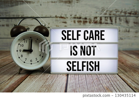 Self Care Is Not Selfish text on light box with alarm clock on wooden background Self Care Is Not Selfish text on light box with alarm clock on wooden background 130435114