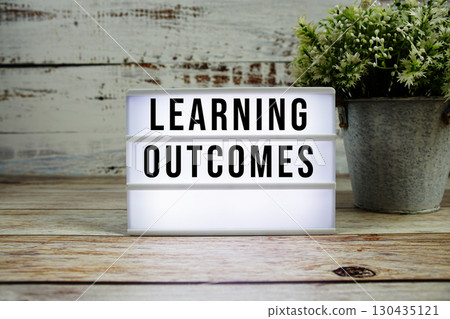 Learning Outcomes text on light box with alarm clock on wooden background 130435121
