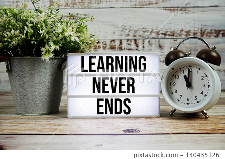 Learning Never Ends text on light box with alarm clock on wooden background 130435126