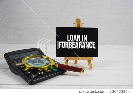 Loan In Forbearance text with magnifying glass and calculator on wooden background 130435264