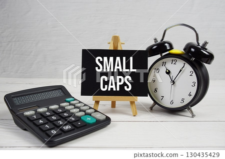 Small Caps text with alarm clock and calculator on wooden background Small Caps text with alarm clock and calculator on wooden background 130435429