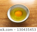 Fresh raw egg with golden yolk and clear egg white in ceramic bowl on wooden table, minimal style food photography highlighting natural texture, cooking ingredient and healthy protein source 130435453