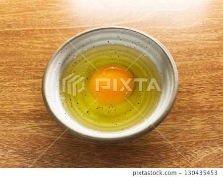 Fresh raw egg with golden yolk and clear egg white in ceramic bowl on wooden table, minimal style food photography highlighting natural texture, cooking ingredient and healthy protein source 130435453