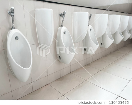 Row of white ceramic urinals in a public restroom, clean and organized sanitary facility with tiled walls and floor, representing hygiene, infrastructure, and modern bathroom interior design Row of white ceramic urinals in a public restroom, clean and organized sanitary facility with tiled walls and floor, representing hygiene, infrastructure, and modern bathroom interior design 130435455
