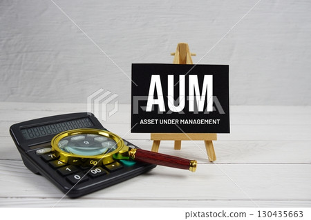 AUM Asset Under Management text with magnifying glass and calculator on wooden background AUM Asset Under Management text with magnifying glass and calculator on wooden background 130435663