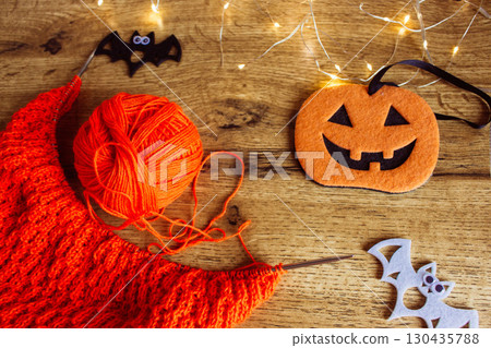 Orange wool and knitting needles with decorative bat. Halloween still life. Cozy lifestyle concept. Autumn lifestyle. October background. Bright needlework and smiling pumpkin. 130435788