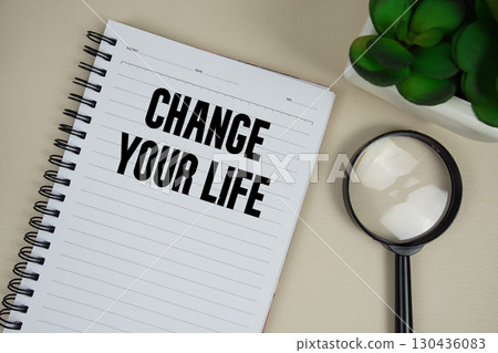 Change Your Life text on paper notebook with magnifying glass on beige leather background 130436083