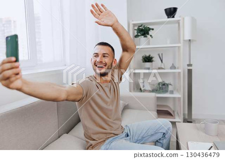 Happy man taking a selfie in a modern living room, showcasing self-expression and joy with a bright and stylish interior amidst a relaxed atmosphere. Happy man taking a selfie in a modern living room, showcasing self-expression and joy with a bright and stylish interior amidst a relaxed atmosphere. 130436479