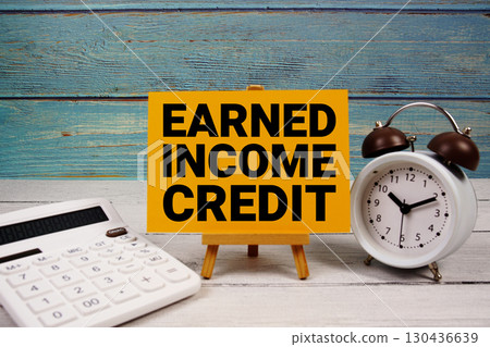 Earned Income Credit text written on paper card with calculator and alarm clock on wooden background Earned Income Credit text written on paper card with calculator and alarm clock on wooden background 130436639