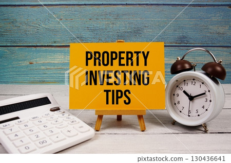 Property Investing Tips text written on paper card with calculator and alarm clock on wooden background Property Investing Tips text written on paper card with calculator and alarm clock on wooden background 130436641