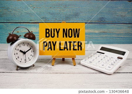 Buy Now Pay Later text written on paper card with calculator and alarm clock on wooden background 130436648