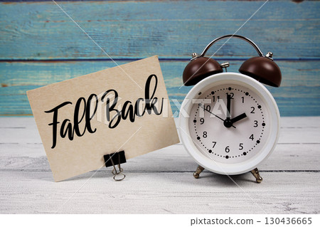 Fall Back text written on paper card with alarm clock on wooden background Fall Back text written on paper card with alarm clock on wooden background 130436665