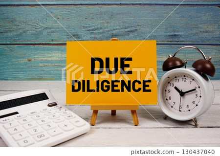 Due Diligence text written on paper card with calculator and alarm clock on wooden background 130437040